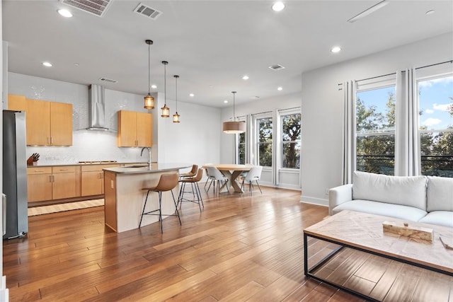 kitchen featuring wood finished floors, visible vents, wall chimney range hood, freestanding refrigerator, and light brown cabinetry