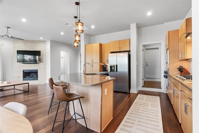 kitchen featuring a tile fireplace, stainless steel appliances, a sink, open floor plan, and dark wood finished floors