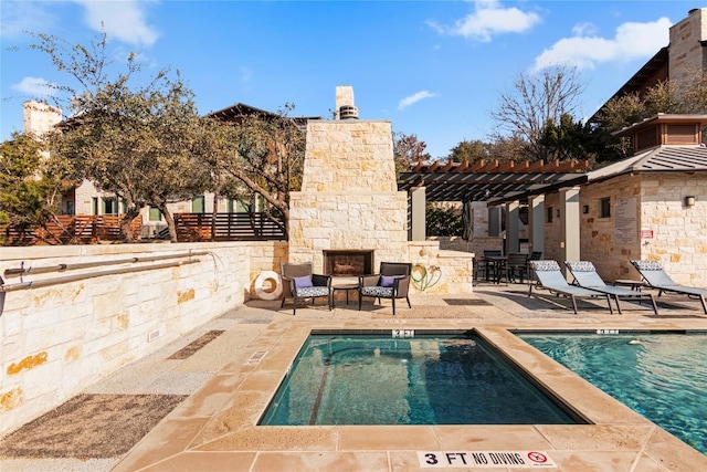 view of swimming pool with an outdoor stone fireplace, a patio area, and a pergola