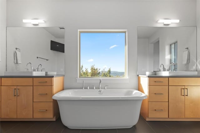 bathroom with a freestanding tub, two vanities, a sink, and tile patterned floors