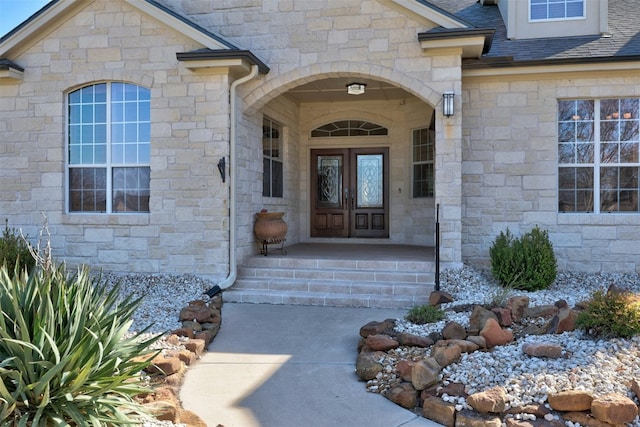 property entrance with stone siding, covered porch, and roof with shingles