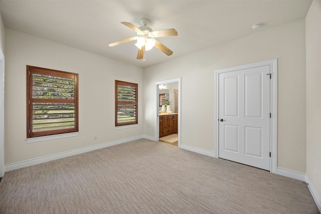 unfurnished bedroom with light carpet, ceiling fan, baseboards, and ensuite bathroom