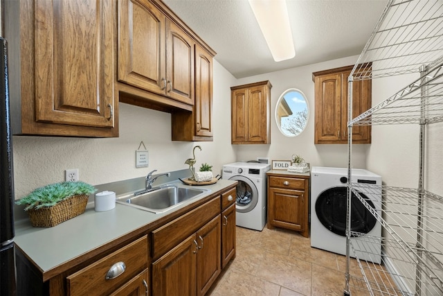 laundry room with cabinet space, a textured ceiling, washer and clothes dryer, and a sink