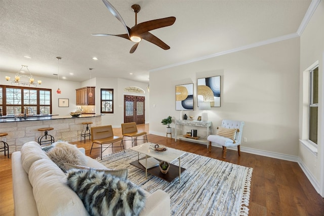 living area featuring a textured ceiling, baseboards, wood finished floors, and ornamental molding