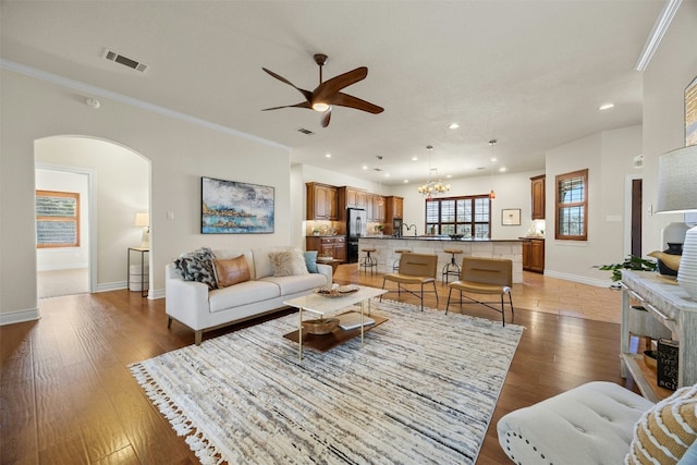 living area featuring arched walkways, light wood-style flooring, visible vents, baseboards, and ornamental molding