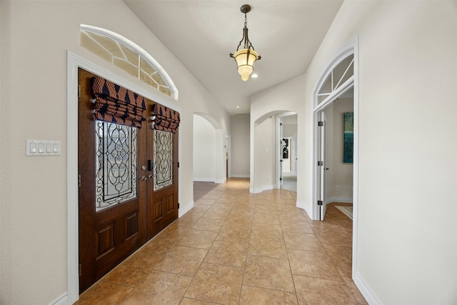 entrance foyer featuring arched walkways, light tile patterned flooring, and baseboards