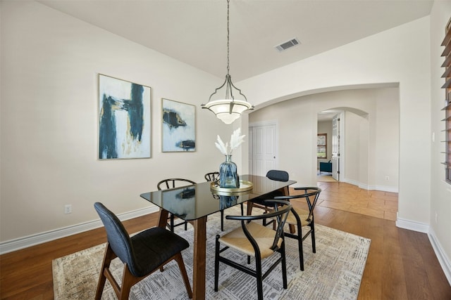 dining area with arched walkways, dark wood finished floors, lofted ceiling, visible vents, and baseboards