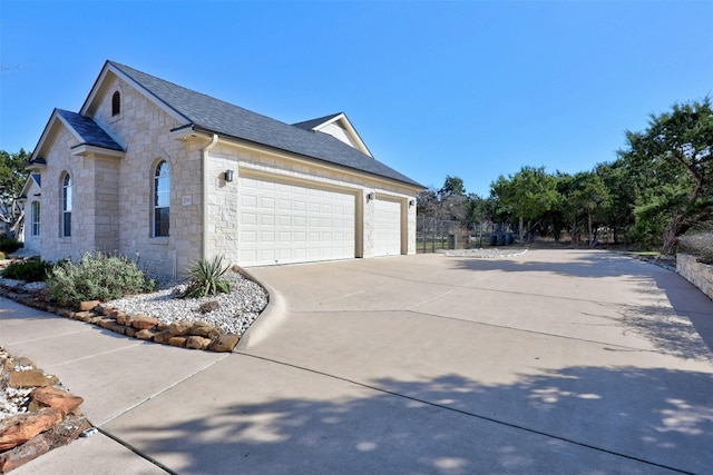 view of side of property with a shingled roof, stone siding, driveway, and an attached garage