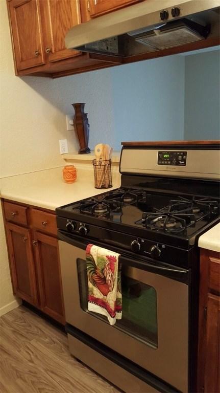 kitchen featuring stainless steel range with gas cooktop, brown cabinets, light countertops, light wood-style floors, and under cabinet range hood