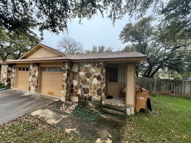 view of front of home with an attached garage, stone siding, driveway, and fence