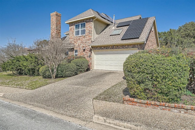 traditional-style house with roof with shingles, concrete driveway, a garage, brick siding, and roof mounted solar panels