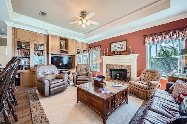 living room with a raised ceiling, plenty of natural light, visible vents, and light wood-type flooring