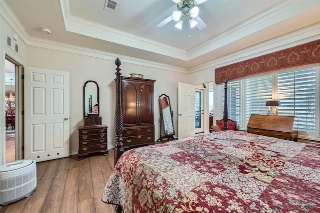 bedroom featuring a tray ceiling, crown molding, visible vents, and light wood finished floors