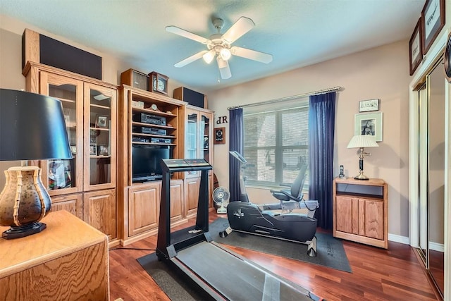 exercise room with dark wood finished floors, baseboards, and a ceiling fan