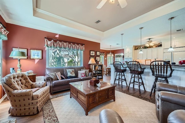 living room featuring light wood finished floors, visible vents, crown molding, and a tray ceiling