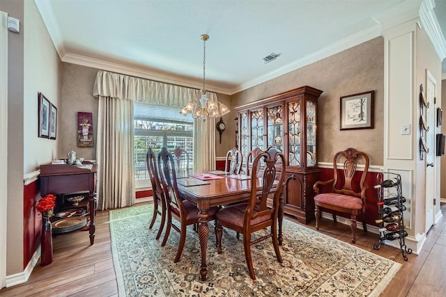 dining area with baseboards, visible vents, light wood finished floors, an inviting chandelier, and crown molding