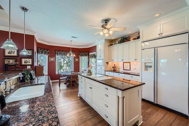 kitchen with dark wood finished floors, built in appliances, ornamental molding, white cabinetry, and a sink