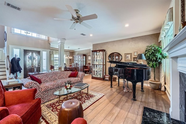 living room featuring visible vents, light wood-style flooring, decorative columns, ornamental molding, and ceiling fan with notable chandelier