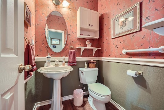 half bathroom featuring baseboards, toilet, wood finished floors, and wallpapered walls