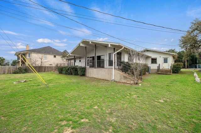 rear view of house with fence, central AC unit, and a lawn