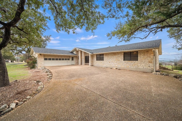 ranch-style home with concrete driveway, stone siding, an attached garage, and a shingled roof