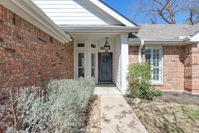 doorway to property with roof with shingles and brick siding