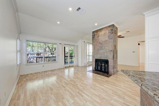 unfurnished living room featuring a tile fireplace, visible vents, vaulted ceiling, light wood-type flooring, and crown molding