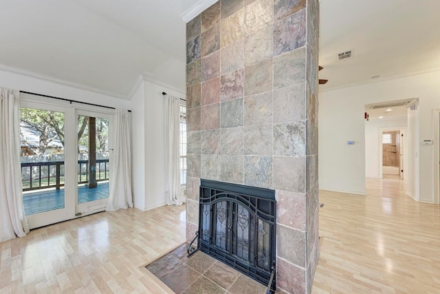 living area with ornamental molding, a tile fireplace, visible vents, and wood finished floors