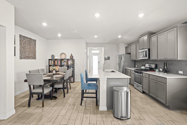 kitchen featuring a sink, stainless steel appliances, gray cabinets, and a kitchen island with sink