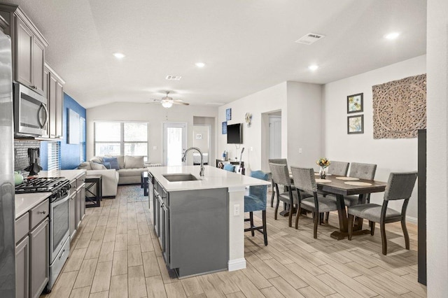 kitchen with a sink, visible vents, appliances with stainless steel finishes, wood tiled floor, and a center island with sink