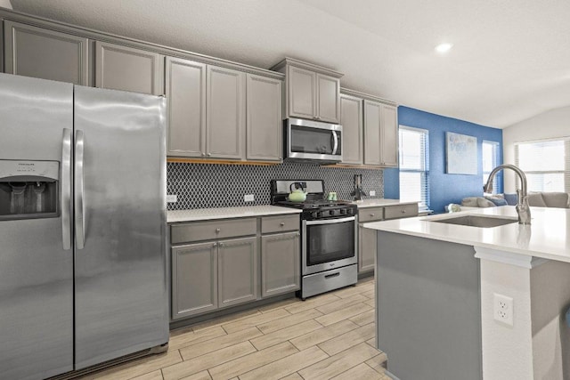 kitchen featuring stainless steel appliances, tasteful backsplash, light countertops, gray cabinetry, and a sink