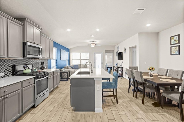 kitchen featuring gray cabinetry, a sink, visible vents, open floor plan, and appliances with stainless steel finishes