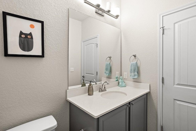 bathroom with a textured wall, vanity, and toilet