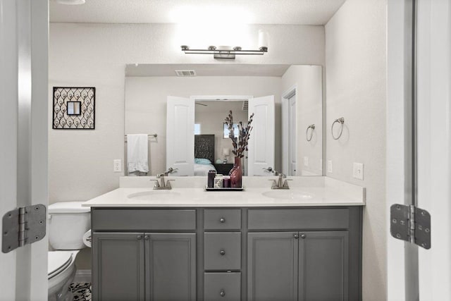 bathroom featuring toilet, double vanity, visible vents, and a sink