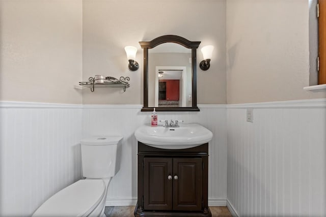 half bathroom with wainscoting, vanity, and toilet