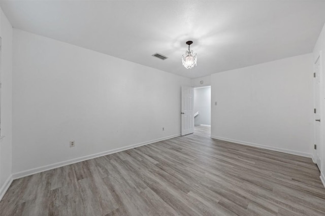 empty room featuring a notable chandelier, wood finished floors, visible vents, and baseboards