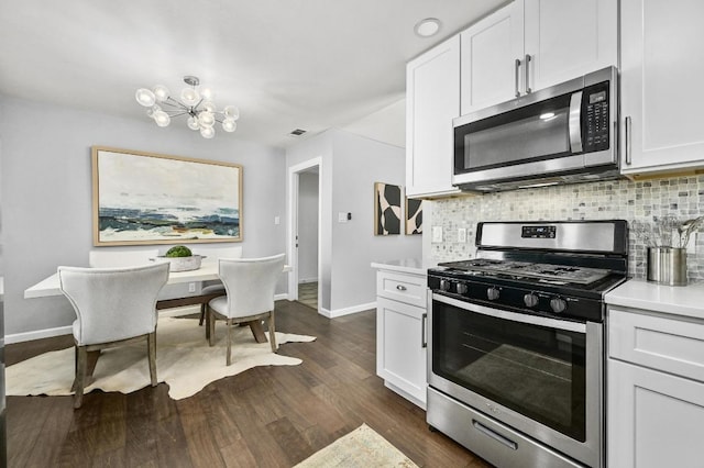 kitchen with dark wood finished floors, stainless steel appliances, light countertops, decorative backsplash, and a chandelier