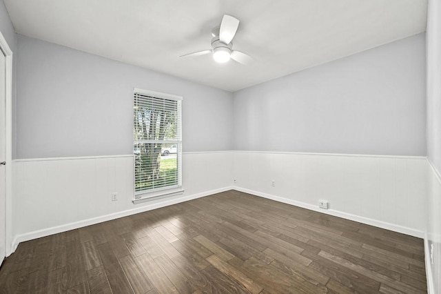 empty room featuring a wainscoted wall, a ceiling fan, and dark wood-style flooring