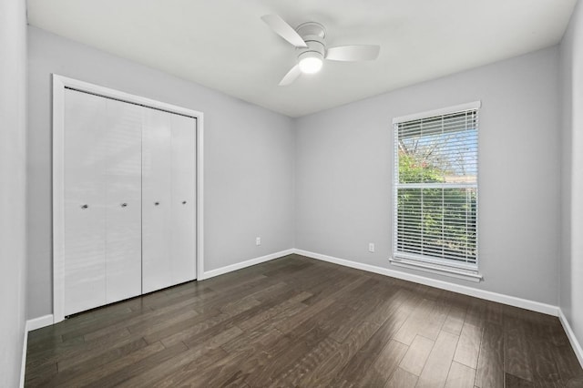 unfurnished bedroom with dark wood-type flooring, a closet, a ceiling fan, and baseboards