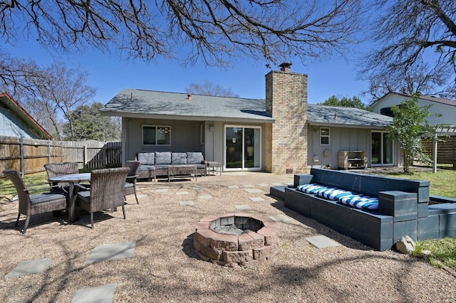 back of house with an outdoor living space with a fire pit, a chimney, fence, a patio area, and board and batten siding