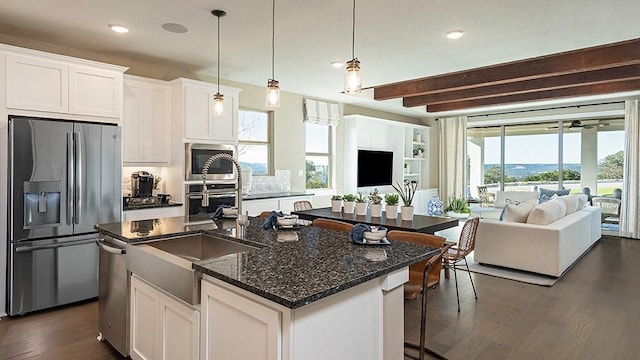 kitchen with white cabinets, appliances with stainless steel finishes, open floor plan, dark wood-type flooring, and a kitchen island with sink