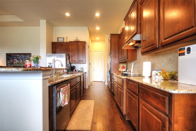 kitchen with dark wood-style flooring, decorative backsplash, appliances with stainless steel finishes, light stone countertops, and under cabinet range hood