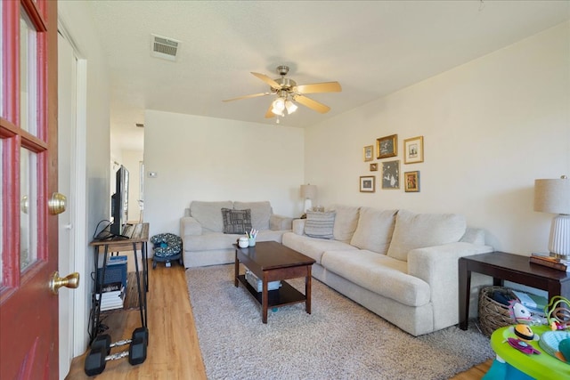 living room with light wood finished floors, visible vents, and a ceiling fan