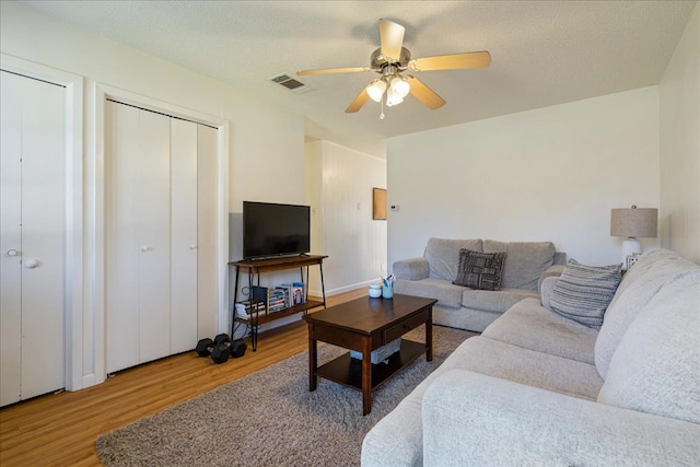 living area featuring ceiling fan, a textured ceiling, wood finished floors, and visible vents