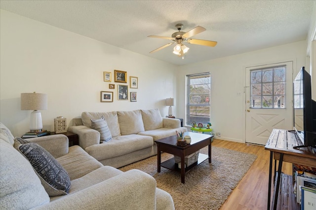 living area with light wood-style flooring, a textured ceiling, baseboards, and a ceiling fan