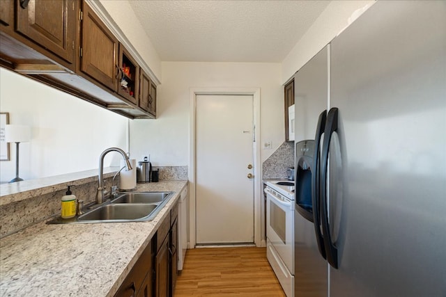 kitchen with electric stove, stainless steel fridge with ice dispenser, light countertops, light wood-type flooring, and a sink