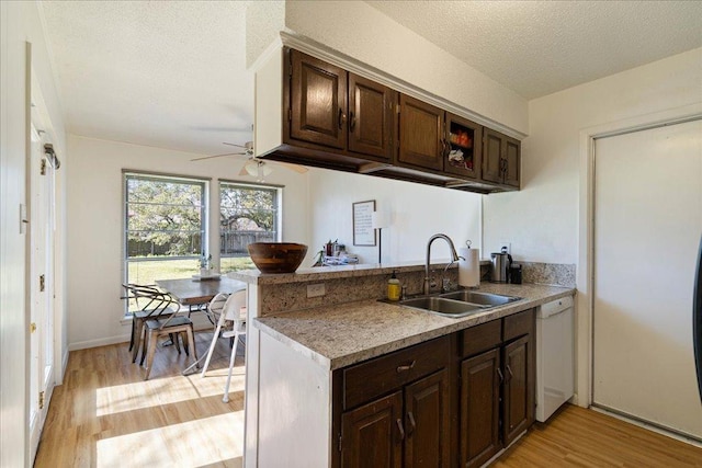 kitchen featuring a peninsula, white dishwasher, a textured ceiling, light wood-type flooring, and a sink