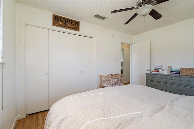 bedroom with a closet, visible vents, a ceiling fan, a textured ceiling, and wood finished floors