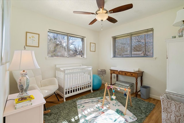 bedroom featuring a ceiling fan, a textured ceiling, wood finished floors, a nursery area, and baseboards