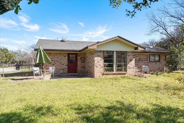 rear view of property featuring a patio, brick siding, a lawn, and fence